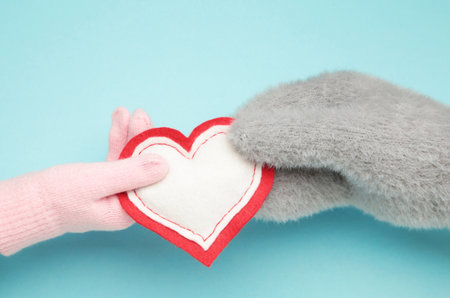 Female hands in warm mittens gives a heart children's hand in gloves on blue background. Top viewの写真素材
