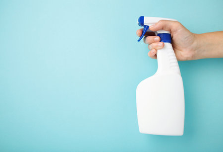 A hand holds a spray of cleaning fluid on blue background. Space for text