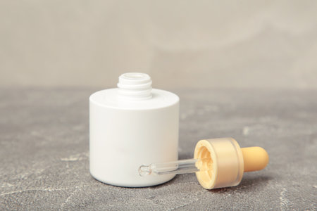 Minimalist white cosmetic dropper bottle on gray background. Elegant mockup for skincare, serum, or beauty branding presentations. Top viewの写真素材