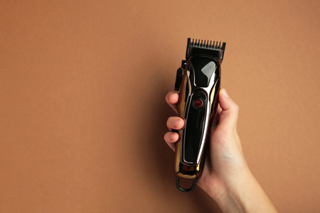 Hair clipper in hand on brown background. Modern hair clipper. Top viewの写真素材