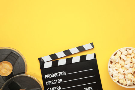 Movie clapper with popcorn and film reels on yellow background. Space for text