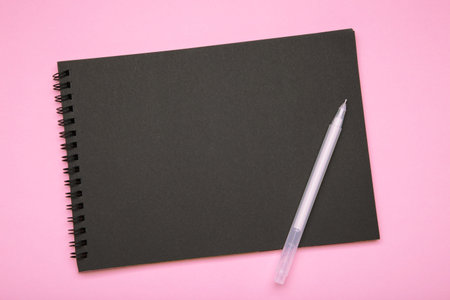 Black notebook with pen on pink background.