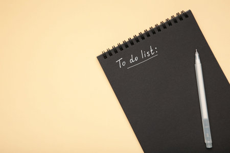 To do list on black notebook with white pen on beige background. Top view