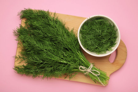 Bunch of green dill and dill on white bowl on pink background. Top view
