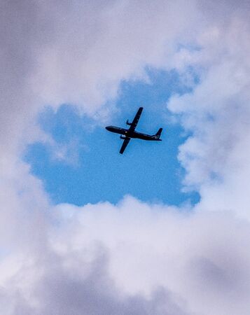 The plane is visible through a hole in the clouds. The plane flies over the city in the clouds. Airplane on sky background.の写真素材