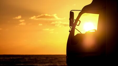 He stopped the car in the evening on the seashore. A truck is parked on the beach. The sun shines in the cockpit.の写真素材