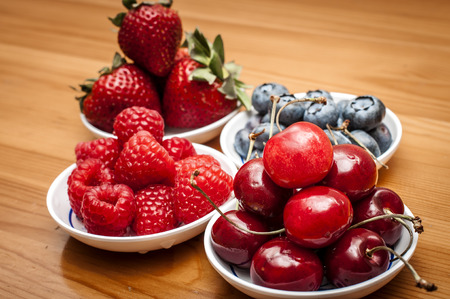 Small bowls of fruit containing cherries, strawberries, blueberries and rasberries on a wooden tableの写真素材