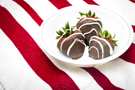 chocolate covered strawberries in a white bowl on a red and white table clothの写真素材