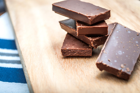 Chocolate pieces stacked on a wooden table and a kitchen tableの写真素材