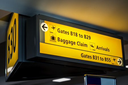Yellow airport signage suspended by the ceiling in a terminal, telling passengers important information about their gates, where baggage claim, departures and arrivals are, etcの写真素材