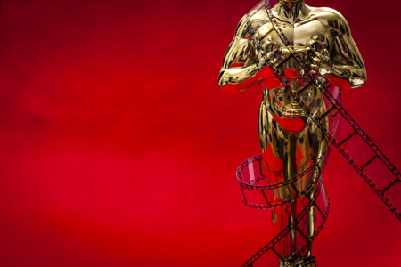 Hollywood film awards concept with shiny metallic movie award wrapped in celluloid film strip on red carpet with copy spaceの写真素材