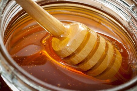 Organic food and healthy diet concept with a macro close up on a wood honey dipper or drizzler pouring aromatic honey into a glass jarの写真素材