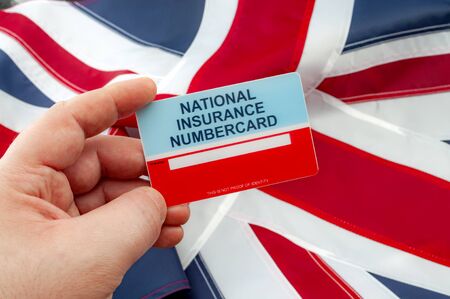 Social security system, access to safety net programs in Great Britain concept theme with a blank National Insurance Number card or NINO held in one hand with the UK flag in the backgroundの写真素材