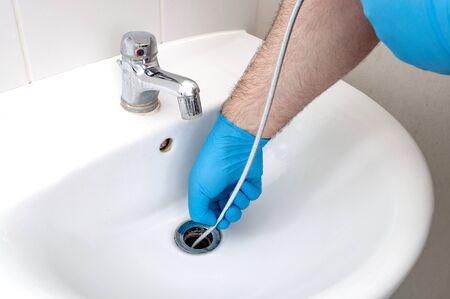 Plumbing issues, occupation in sanitation and handyman contractor concept with plumber repairing drain with plumbers snake (steel spiral that twists through pipes to collect dirt) in residential sinkの写真素材