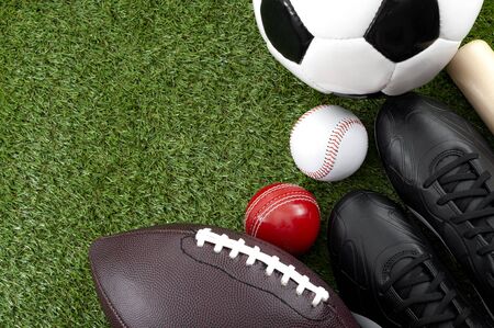 Competitive match and team sports concept with soccer, cricket and american football balls black cleats or sport boots and wooden baseball bat isolated on green grass with copy spaceの写真素材