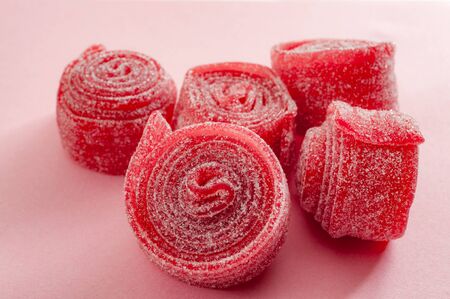 Chewy sweets and strawberry and cherry flavoured gummy candy concept with close up on sweet and sour red sour belts covered in sugar isolated on a pink backgroundの写真素材