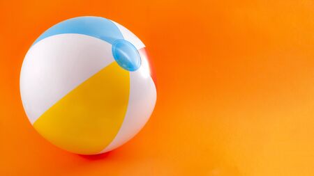 Summer vacation, beach toy and seaside fun activities concept with a inflatable beach ball isolated on orange background with copy spaceの写真素材