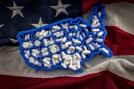 Healthcare, opioid epidemic and drug abuse concept with the map of USA filled with oxycodone and hydrocodone pharmaceutical pills on the American flagの写真素材