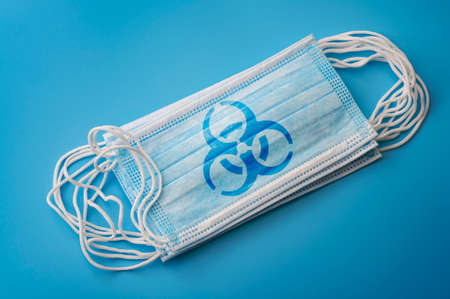 Respiratory sickness infection, novel coronavirus pandemic outbreak and sterile microbiology concept with surgical mask with biohazard logo isolated on blue backgroundの写真素材
