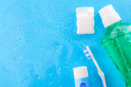 Dental care and oral hygiene concept with a bottle of green mouthwash, toothbrush, dental floss and tube of toothpaste soaked in water droplets, isolated on a blue background with copy space for textの写真素材