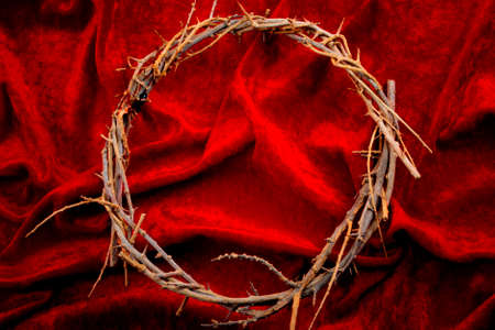 Easter holidays, christian celebration of Jesus resurrection and the Passion of Christ concept with frame made by a crown of thorns on red velvet with dramatic light and copy spaceの写真素材