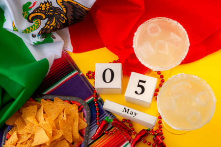 Mexican fiesta and Cinco de Mayo party concept theme with block calendar set on May 5th, jalapeno pepper beads necklace, traditional rug or serape, two margarita glasses, chips and the mexican flagの素材 [FY310166253125]