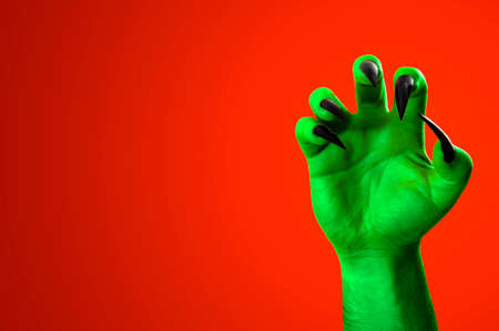 Halloween, nightmare creature and evil monster horror story concept with a scary zombie or demon hand with creepy long black nails isolated on orange background with a clip path cutout and copy spaceの写真素材