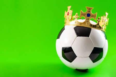 Football is the king of sports, championship winner and league champion concept with a soccer ball wearing a golden crown isolated on green background with copy spaceの写真素材
