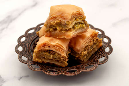 Authentic Middle Easter desserts concept with close up on Turkish baklava on small metal plate beautifully orate with Arabic ornaments isolated on white background with clipping path cutoutの写真素材