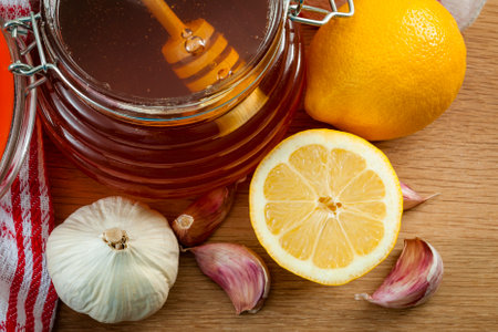 Folk natural remedy for flu and cold, strengthen immunity during winter season, and alternative medicine concept with close up on a jar of honey with a honey dipper, fresh garlic and lemonsの写真素材
