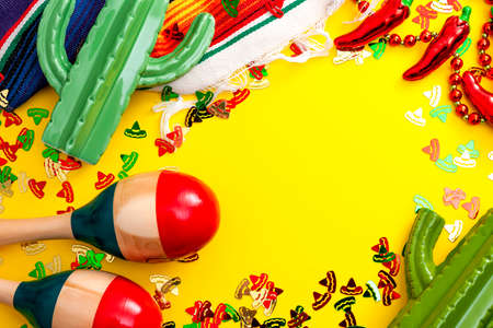 Mexican fiesta and Cinco de Mayo party concept theme with jalapeno pepper necklace, maracas, cactus and traditional rug covered in sombrero shaped confetti on yellow background with copy spaceの写真素材
