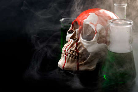 Biological warfare, chemical attack and genocide concept with a skull surrounded by chemistry flasks with smoke or mustard gas coming out of the green liquid with copy spaceの写真素材