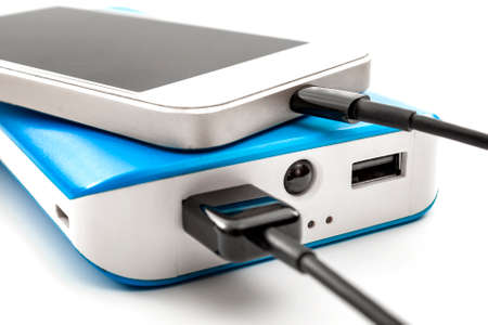 Travel battery recharge, portable energy source and charge your mobile phone anytime and anywhere concept theme with close up on smartphone connected to a blue external power bank with black usb cableの写真素材