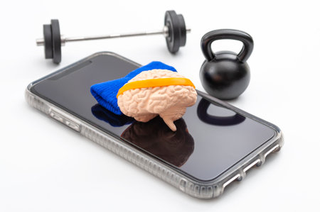 Brain training, neurology improvement app and mind workout concept with human brain with sweatband, barbell and free weights and smartphone isolated on white backgroundの写真素材