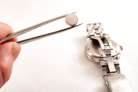 watchmaker is working to replace the battery on an old quartz metal watch in his repair shop, he is holding the new battery in tweezers and getting ready to service the watch on white backgroundの写真素材