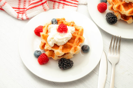 Wholesome breakfast, healthy dessert and waffle snack concept theme with a  plate of belgian waffles with blueberries, blackberries, raspberries and whipped cream on a rustic white wooden tableの写真素材