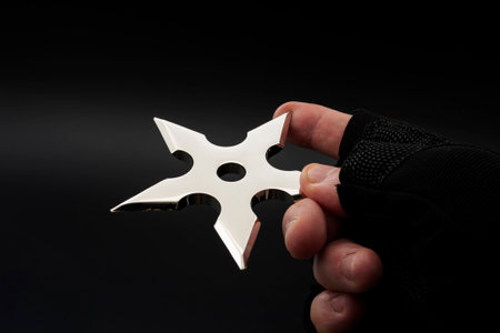 Martial arts skill and traditional Japanese weapon concept with hand in fingerless ninja glove trowing metal star shaped shuriken isolated on black background with copy spaceの写真素材