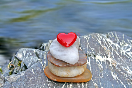 Red Heart on a grey stone on a shore.