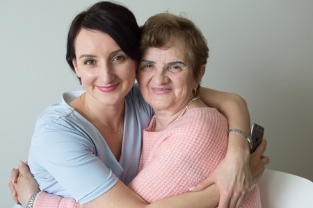 Elderly mother with adult daughter hugging portraitの写真素材
