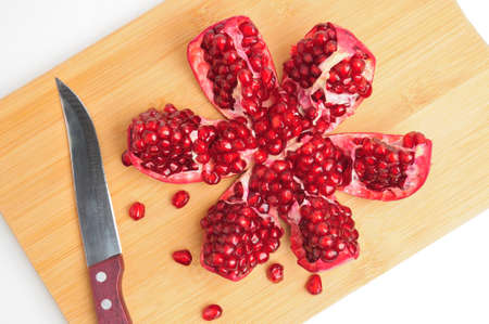 Sliced pomegranate wedges on cutting board with knife on isolated white backgroundの写真素材
