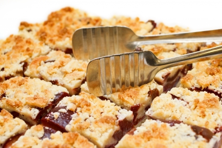Tray of plumb crumble squares with stainless steel tongs and white backgroundの写真素材