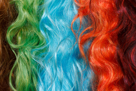 Coloured wigs with long wavy fake hair hanging next to each other.の写真素材