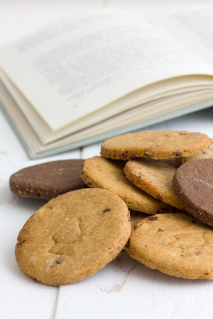Mixed freshly baked biscuits on a rustic white wood table with an open book の写真素材