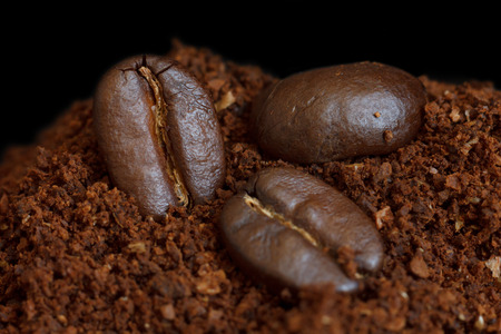Three roasted coffee beans on ground coffee. Black background.の写真素材