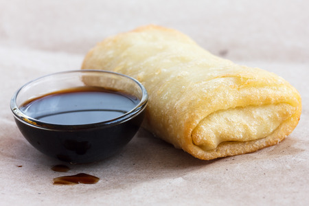 Single fried vegetable spring roll on wax paper with soy sauce.