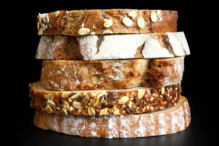 Mixed slices of health breads stacked. On black surface.