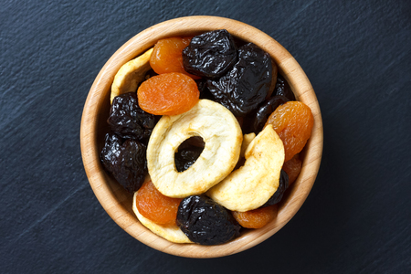 Wooden bowl of mixed dried fruit isolated on dark wood. From above.の写真素材
