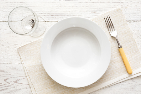 Empty white round soup or pasta plate with fork, placemat and glass. On white wood from above.の写真素材