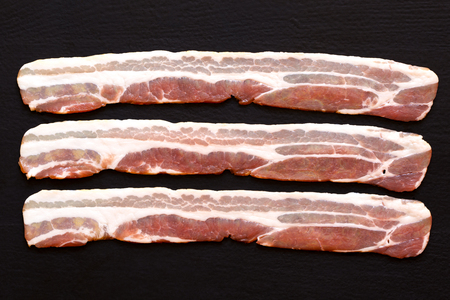 Three strips of streaky uncooked bacon isolated on black  from above.の写真素材