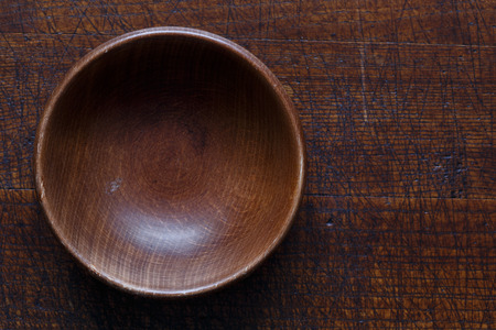 Brown empty wooden bowl isolated on dark wood from above.の写真素材
